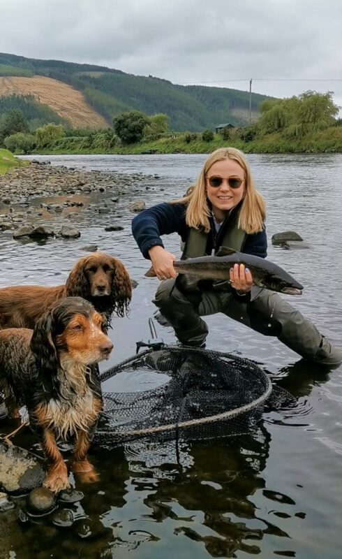 Abby Douetil with a small coloured fish, and photobombed by soggy spaniels

